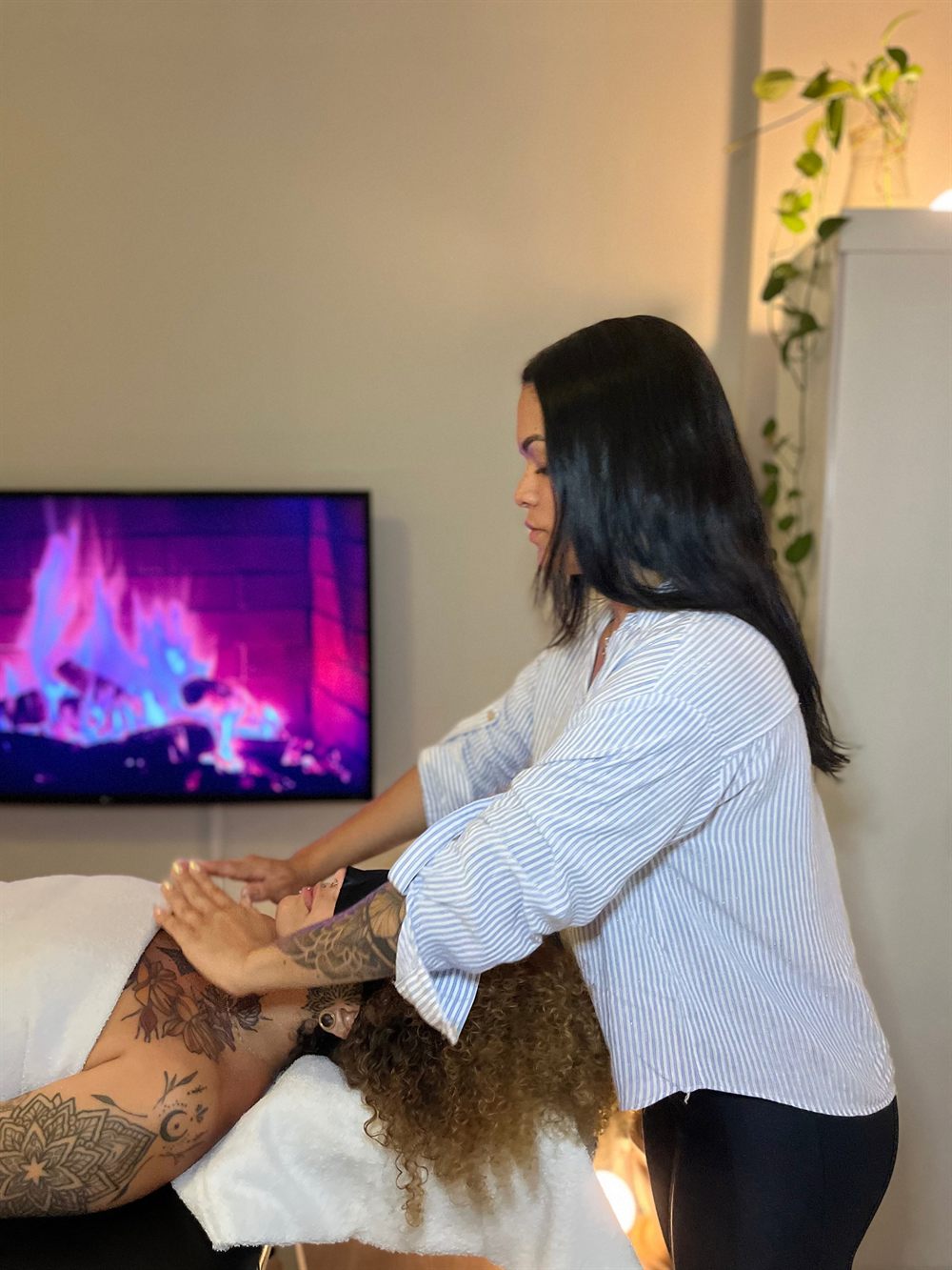 Ramony Santos realizando massagem nas costas de um cliente em sala acolhedora com iluminação suave